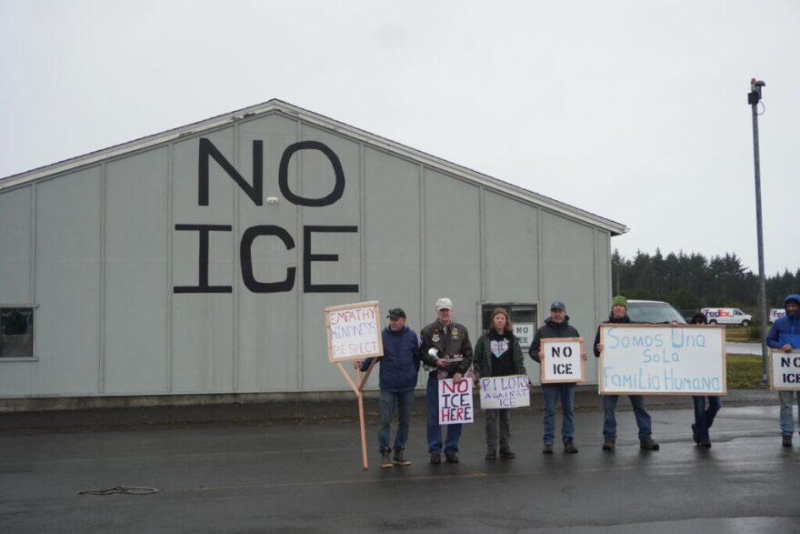 A group of local pilots and organizers stand by a hangar they have painted with “NO ICE”. “We are one human family,” a sign in Spanish held by one demonstrator reads.