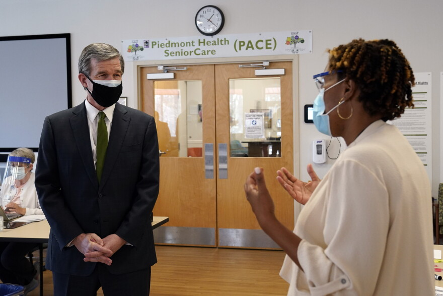 Gov. Roy Cooper, left, speaks with Misty Drake, Chief Operating Officer at Piedmont Health Senior Care, a federally qualified health center where PACE patients (Program of All-Inclusive Care for the Elderly) and underserved populations can receive the COVID-19 vaccine Thursday, Jan. 28, 2021 in Pittsboro, N.C. 