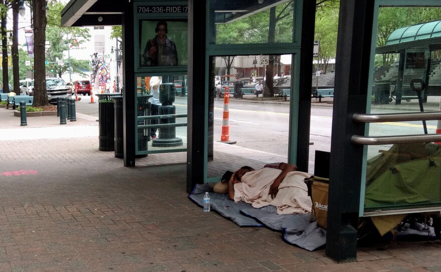 A homeless man sleeps in a bus shelter on East Trade Street during last May's Speed Street Festival uptown. 