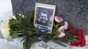 a black and white picture of a smiling man is surrounded by red, pink and white flowers on a snow-covered ground