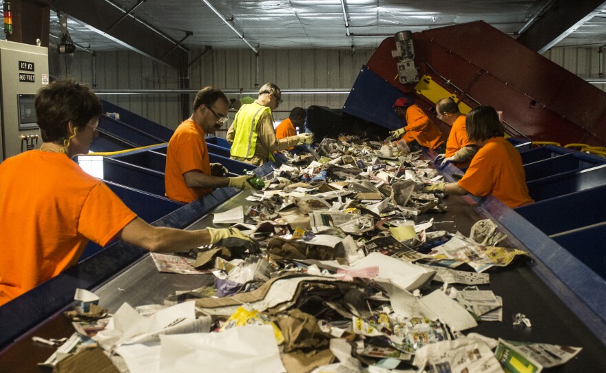 Workers in orange shirts sort cardboard and paper.