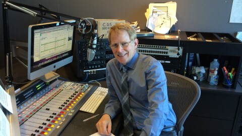 Alan McLellan smiles, seated at a radio control desk.