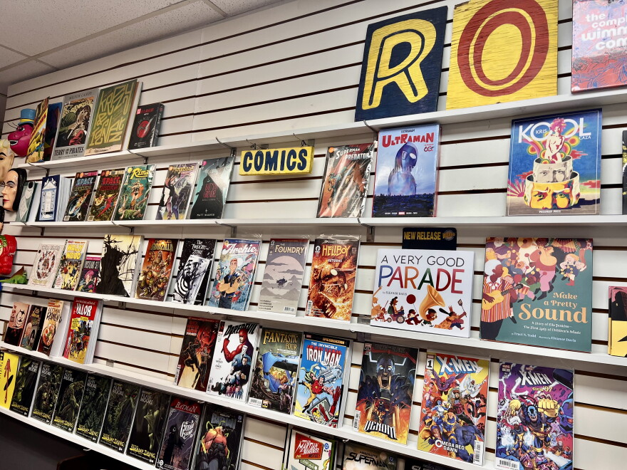 A wall display inside a comic shop features rows of comic books on shelves.