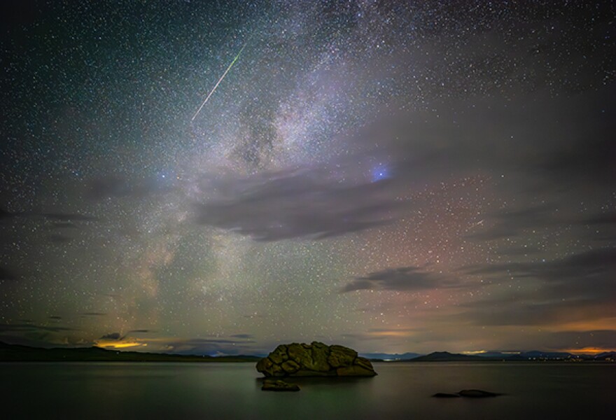 A nighttime photo of stars and the milky way illuminating a lake.
