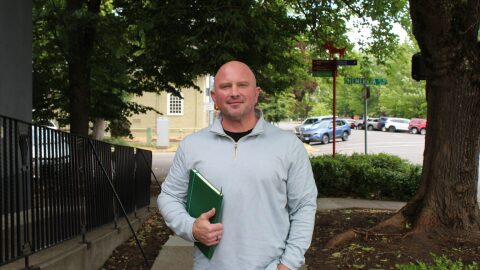 Jason Faler stands on sidewalk with a notebook under his arm.
