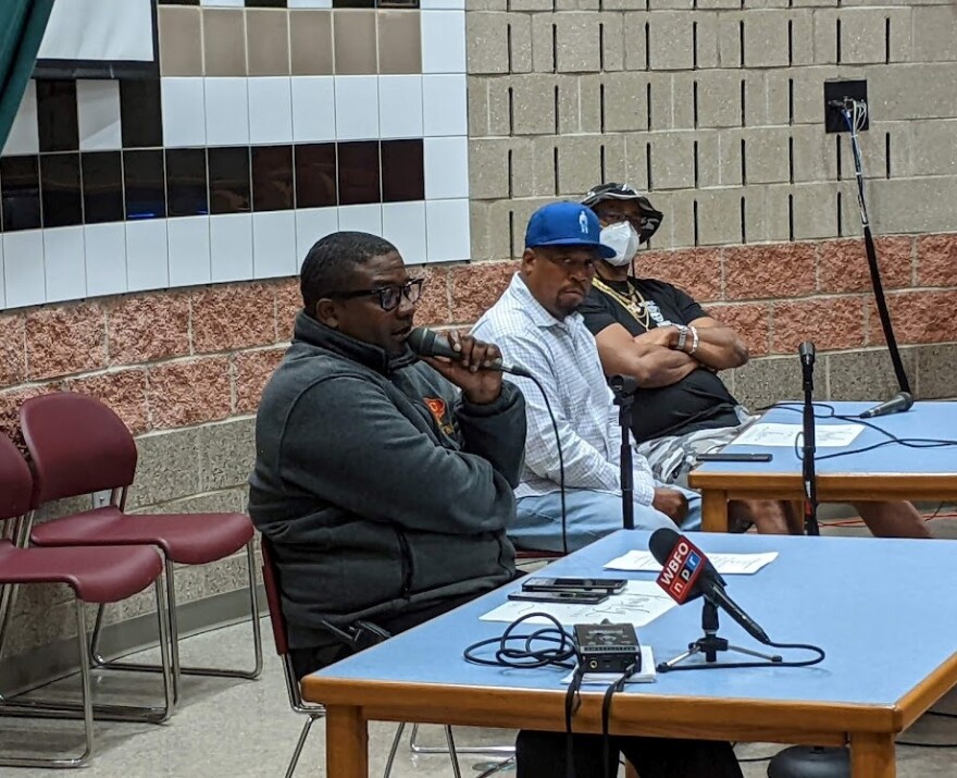 Three men sitting at a table. One is speaking into a microphone.