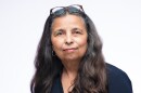 Portrait of a woman with a white background looking straight ahead at the camera. 