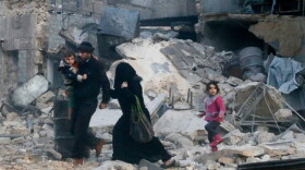 People walk on rubble of collapsed buildings at a site hit by what activists said was barrel bombs dropped by government forces in Aleppo's Dahret Awwad neighborhood January 29, 2014.
