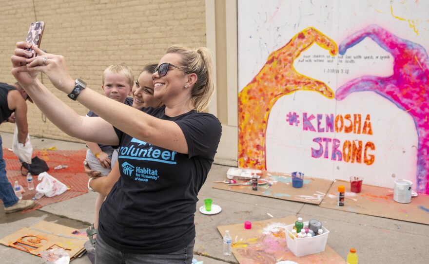 Angela Elliott (C) takes a picture in front of a mural she helped to create on the boarded windows of a business in the Uptown neighborhood of Kenosha, WI on August 28.