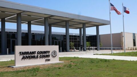 On the left, a sign in front of a building reads "Tarrant County Juvenile Court." On the right, the American and Texas flags fly. 