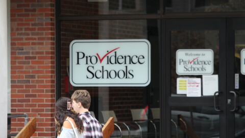 Students walk past a Providence Public Schools sign. The district continues to struggle with low reading and math scores as questions about its leadership emerge after seven years of state control. Credit: Ben Berke/Ocean State Media
