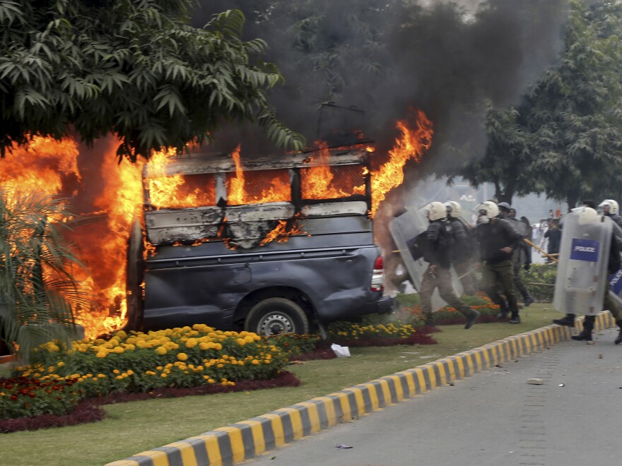 Police officers gather next to a burning police vehicle set on fire by angry lawyers during clashes in Lahore, Pakistan, on Wednesday.