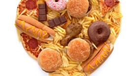 Various types of unhealthy food in the shape of a heart over a white background