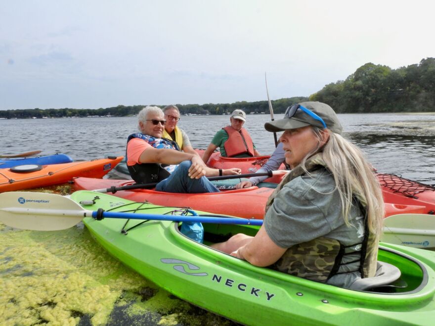 Four people are sitting in three different kayaks. There is a woman in a green one in the forefront. 