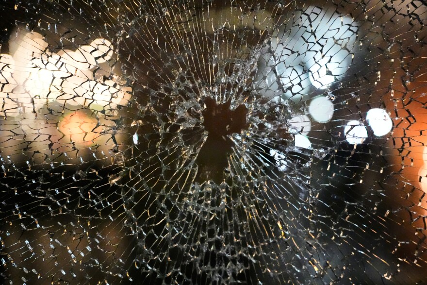 A window is shown shattered with lights reflecting onto the glass.