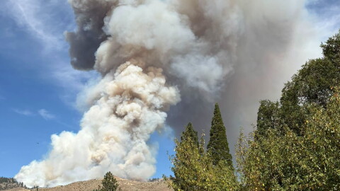 Wildfire smoke fills the sky behind rolling hills.