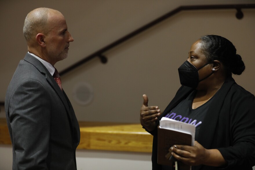 a woman with a mask on speaking with Hillsborough Superintendent Addison Davis about redistricting in a large auditorium.