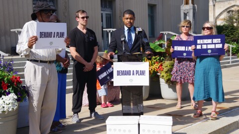 Kalamazoo Forward Executive Director Chokwe Pickford speaks in front of Kalamazoo City Hall on Wednesday, July 1. In front of him sits boxes of petition signatures for a healthcare ballot initiative.