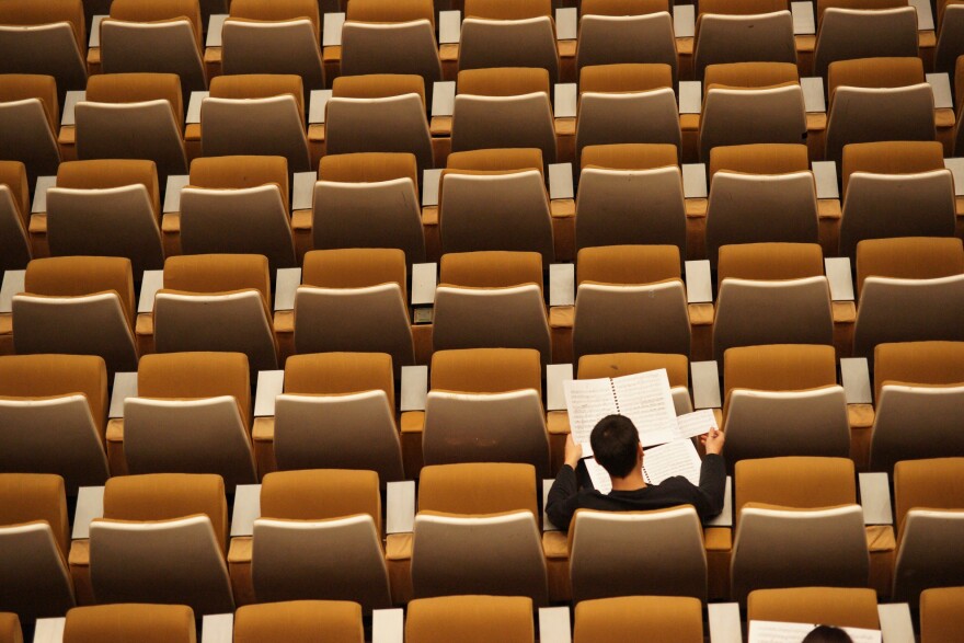 A student studies alone in a large array of empty chairs in a classrom.