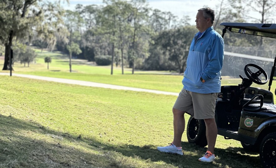 Dudley Hart stands near a team golf cart as he watches the tee shot on the 17th hole.