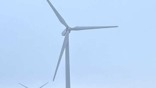 Three large wind turbines in farm fields with snow on the ground. 