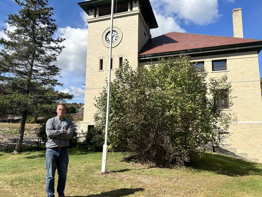 A man stands in front of a building and a flagpole