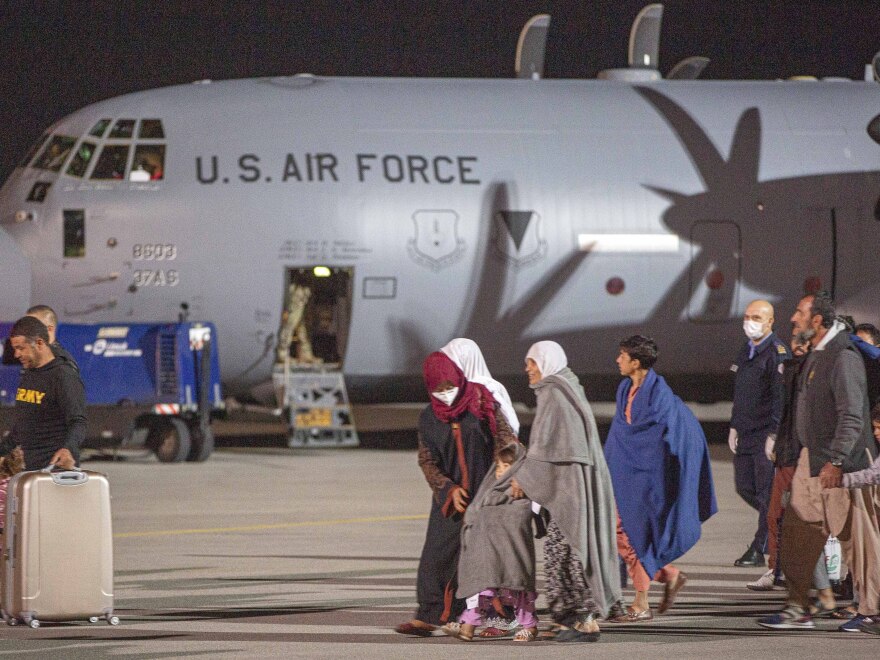 Families evacuated from Kabul walk past a U.S Air Force plane that flew them to Pristina International Airport in Kosovo on Sunday.