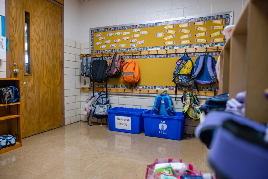 Backpacks hang on a rack outside a classroom.