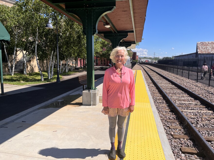 A woman in a pink shirt stands on a train platform in downtown Burlington.