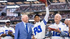 Dallas Cowboys owner Jerry Jones present commemorative footballs to former receiver Drew Pearson, center, and quarterback Roger Staubach, right, in honor of the 50th anniversary of their "Hail Mary" pass before a football game between the Cowboys and the Washington Commanders, Sunday, Oct. 19, 2025, in Arlington, Texas. (Jeffrey McWhorter/AP)