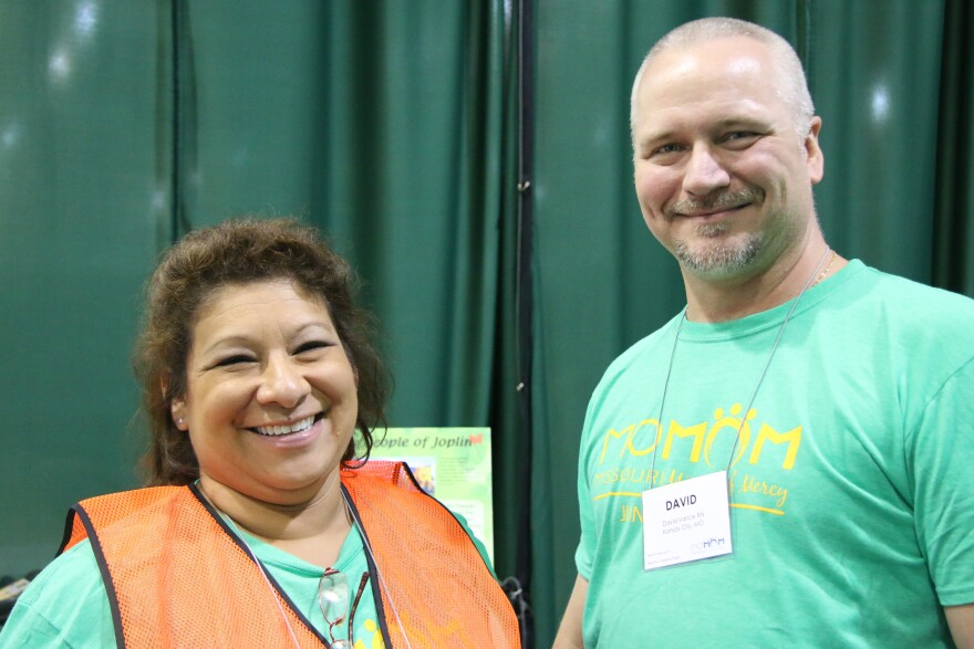 Debbie Vance, left, smiles into the camera and wears a green MOMOM shirt and an orange vest. Her husband, David Vance, also wears a green MOMOM shirt and smiles into the camera.