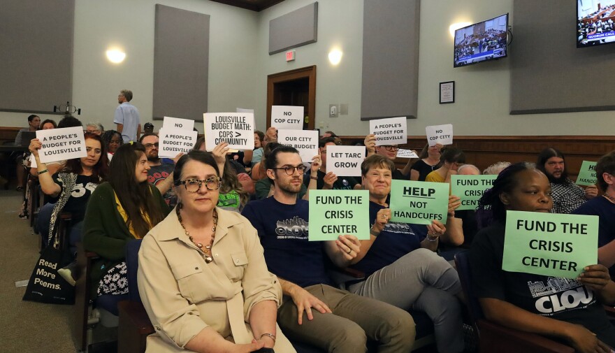Louisville residents hold signs in the gallery of Metro Council chambers
