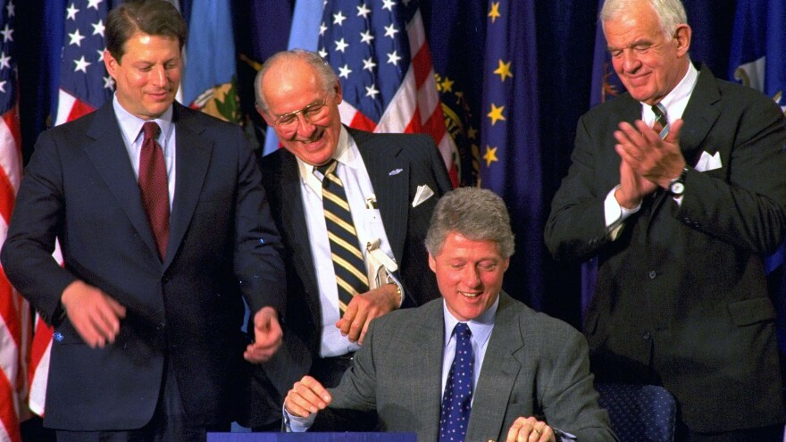 House Minority Leader Bob Michel (center) looks over President Clinton's shoulder as he signs legislation implementing the North American Free Trade Agreement. Vice President Al Gore (left) and House Speaker Thomas Foley also look on.