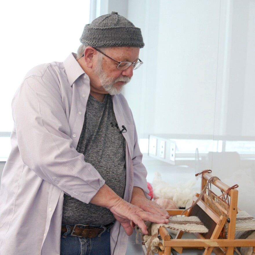 A man demonstrates how to weave fabric with a loom.