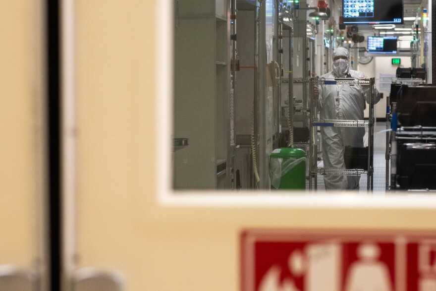 A person in a full-body clean suit walks a cart down a hallway.