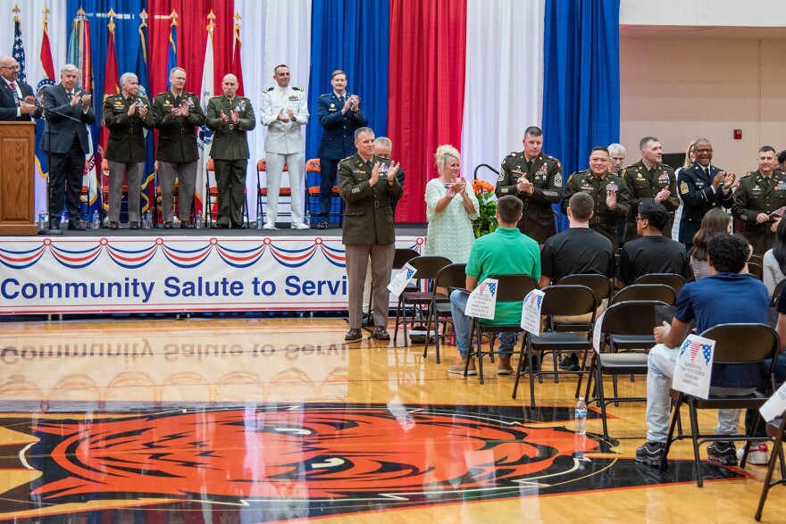 Military and community leaders, including Missouri Gov. Mike Parson (second from left), applaud new military recruits at a "Community Salute to Service" May 11 at Waynesville, Mo. High School.