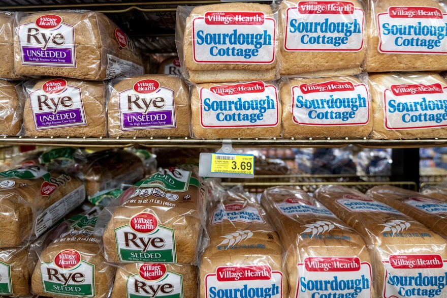 Shelves of packaged Village Hearth sourdough cottage and rye bread loaves, with a price tag of $3.69 visible.