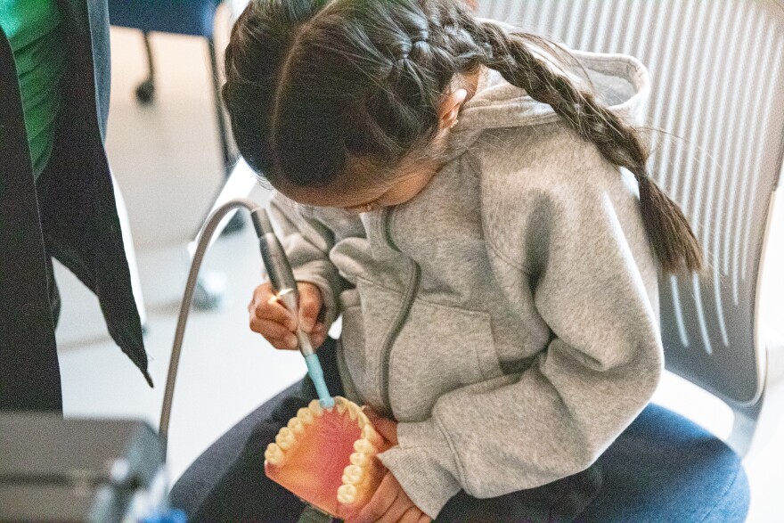 A girl practices polishing teeth at a spring break camp.