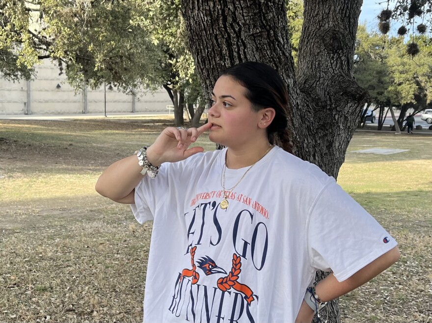 A young college student wearing a UTSA "Let's Go 'Runners" t-shirt looks towards the building where they take most of their classes.
