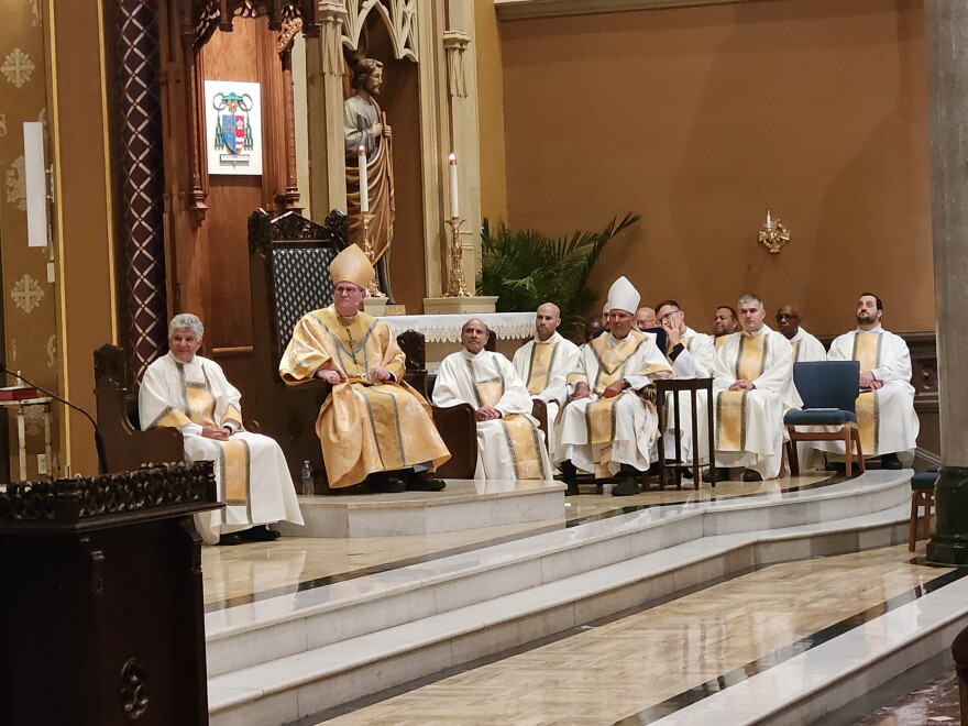 A number of Catholic clergy sit and listen to a speech off camera.