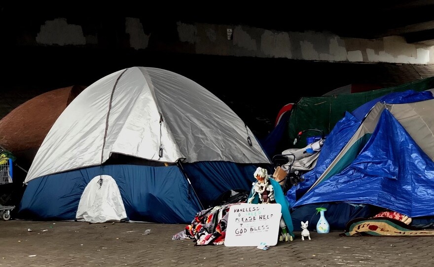  Tents on sidewalk with a sign reading "homeless, need help, God bless"