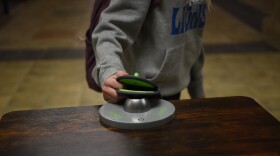 Grayling High School student Mayce McClain locks her Yondr pouch at one of the school’s bases. Cell phones are placed inside the pouch, which is magnetically locked during the school day. Grayling High Principal Sarah Allen said that, with the pouches, it’s “black and white,” making enforcement of the policy easier.