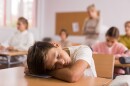 tired school boy lying and sleeping at desk in classroom during lesson