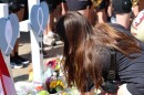 A brown-haired woman crouches in front of crosses and flowers that are part of a memorial recognizing the people killed and injured in the April 2025 FSU school shooting.