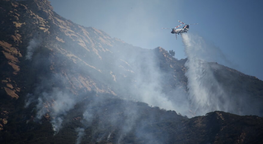A firefighting helicopter makes a water drop on the west side of the Alisal Wildfire Friday.