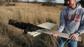 Tyler Lane pulls up a wooden marker covered with oily sludge in the land behind his Bristow home. Lane uses stakes and rope to keep his two children out of the oiliest, most dangerous parts of his property, which sits atop the abandoned Wilcox Refinery, O