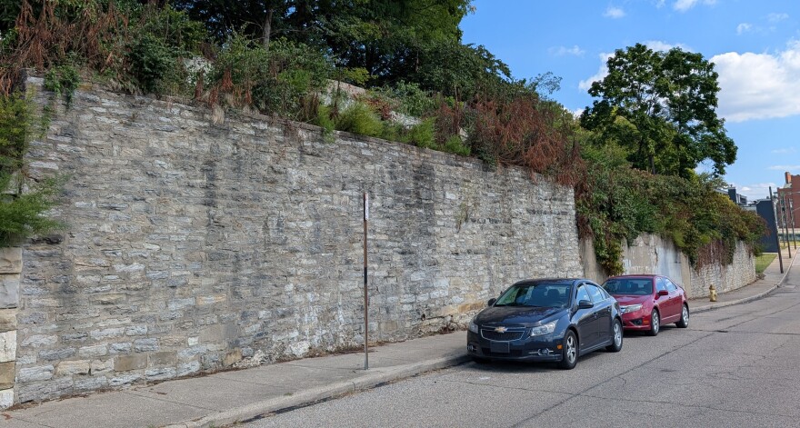 A brick wall along a street with two parked cars. 