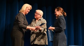 Three women standing on a stage with a blue curtain behind them