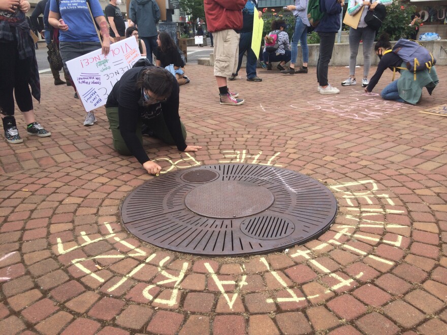 Protesters use colored chalk to write slogans and make drawings on the brick plaza in front of the Collier Center in downtown Medford on Saturday.