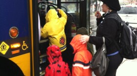 Woman with unbrella helps kids get on a bus